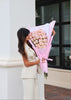 Woman holding a large bouquet of pink roses in front of a building.